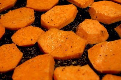 Sweet potato slices with seasoning on baking sheet