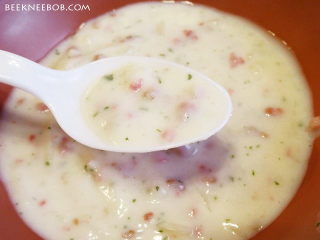 A spoonful of prepared bacon potato chowder hovers over a bowl of chowder