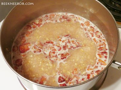 A pot on the stove containing strawberry oatmeal in the middle of the cooking process